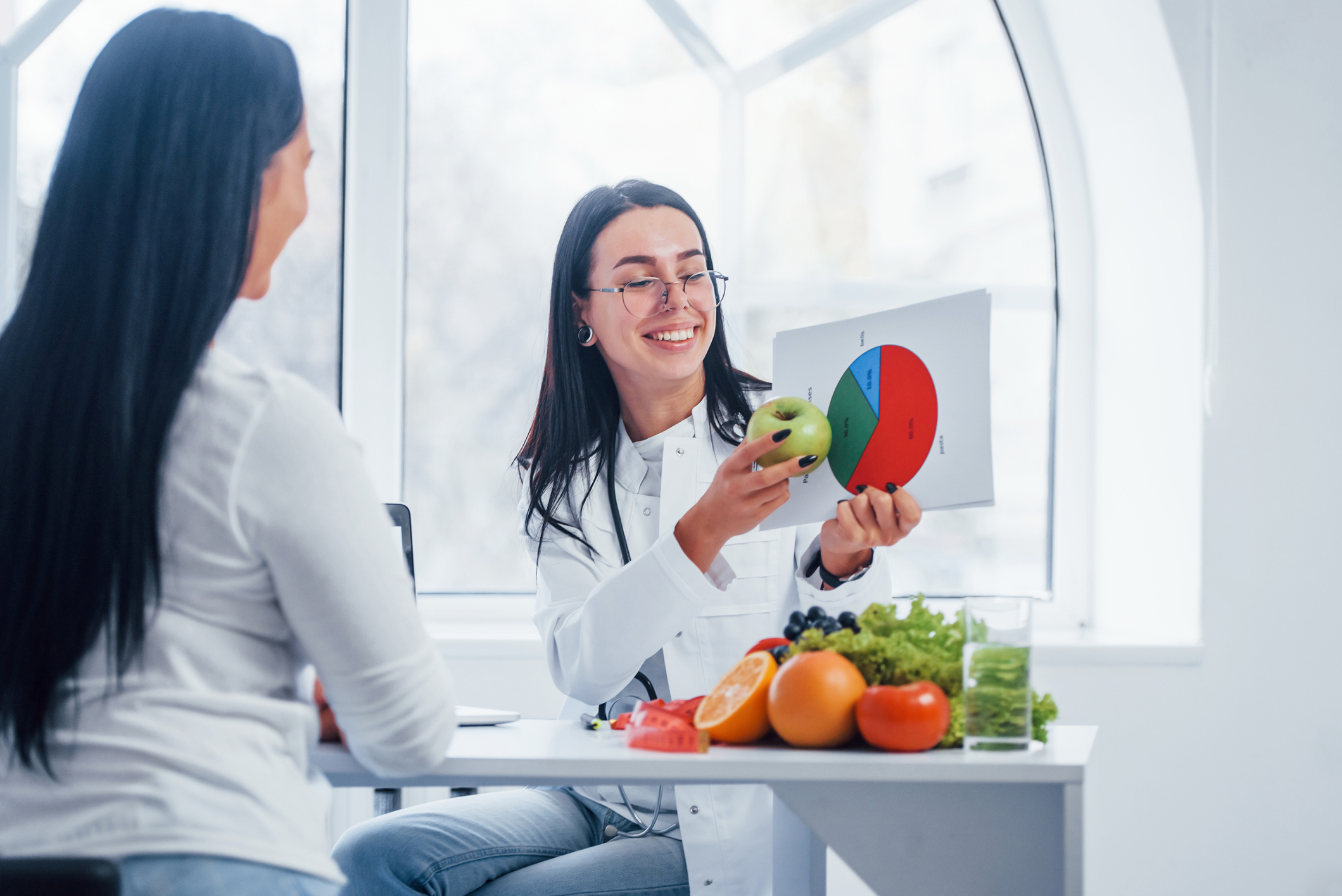 Female nutritionist with graph gives consultation to patient indoors in the office.